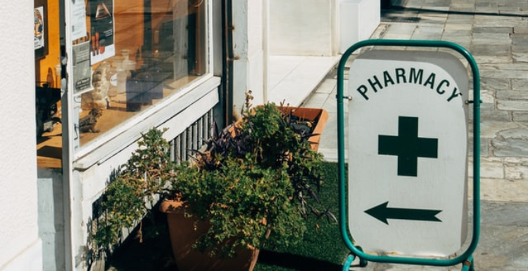 A pharmacy swingboard with a green cross and an arrow pointing to a shop 