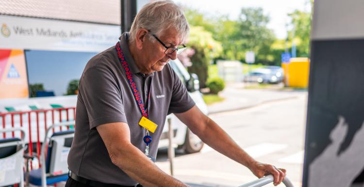 Grey-haired volunteer pushes a trolley outside a hospital