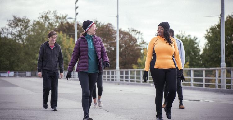 A group of mixed age people, including older people, walking down a road. They are dressed for cold weather. 